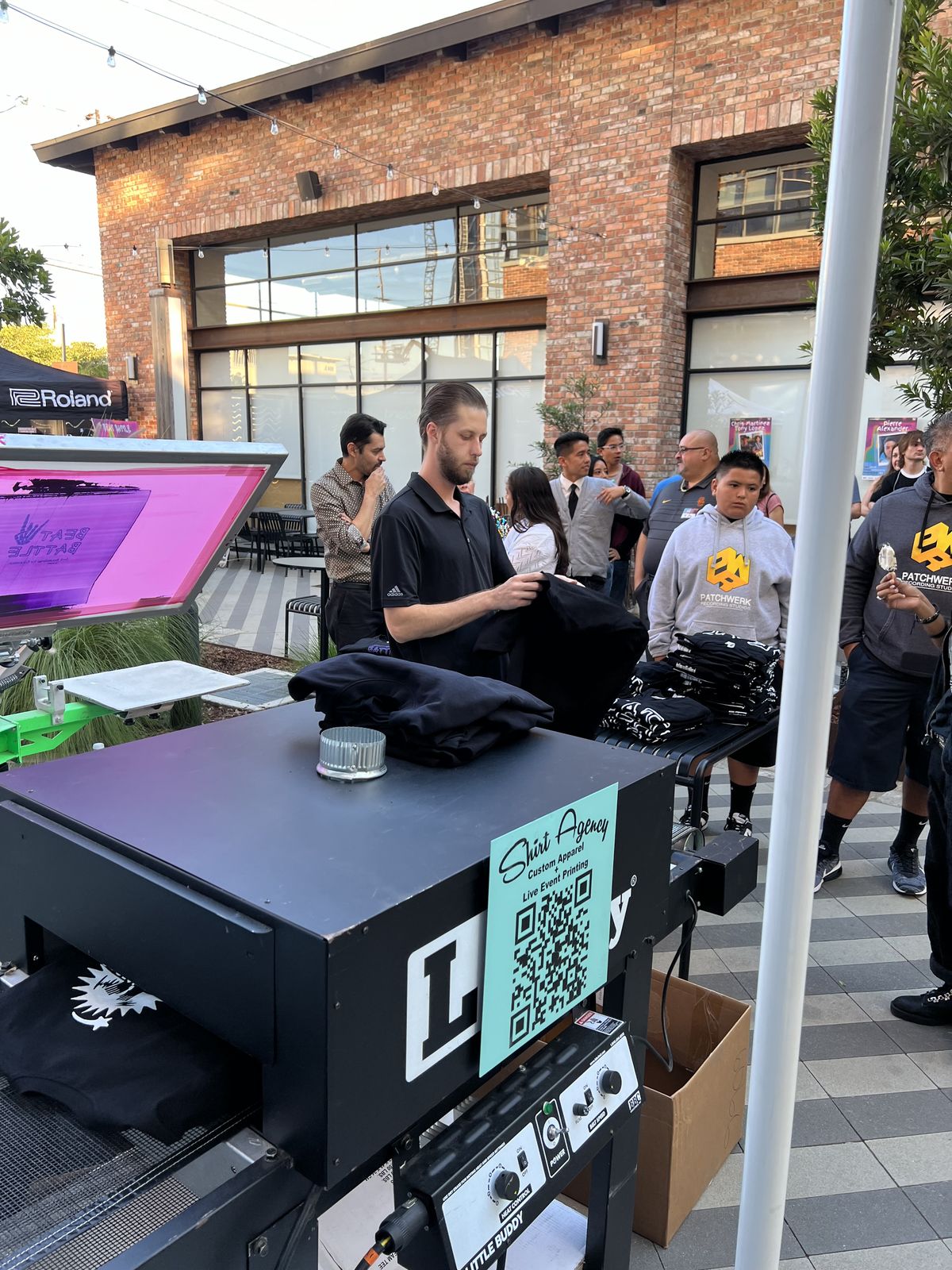 Night market customization station printing and patching merch outside a brick storefront