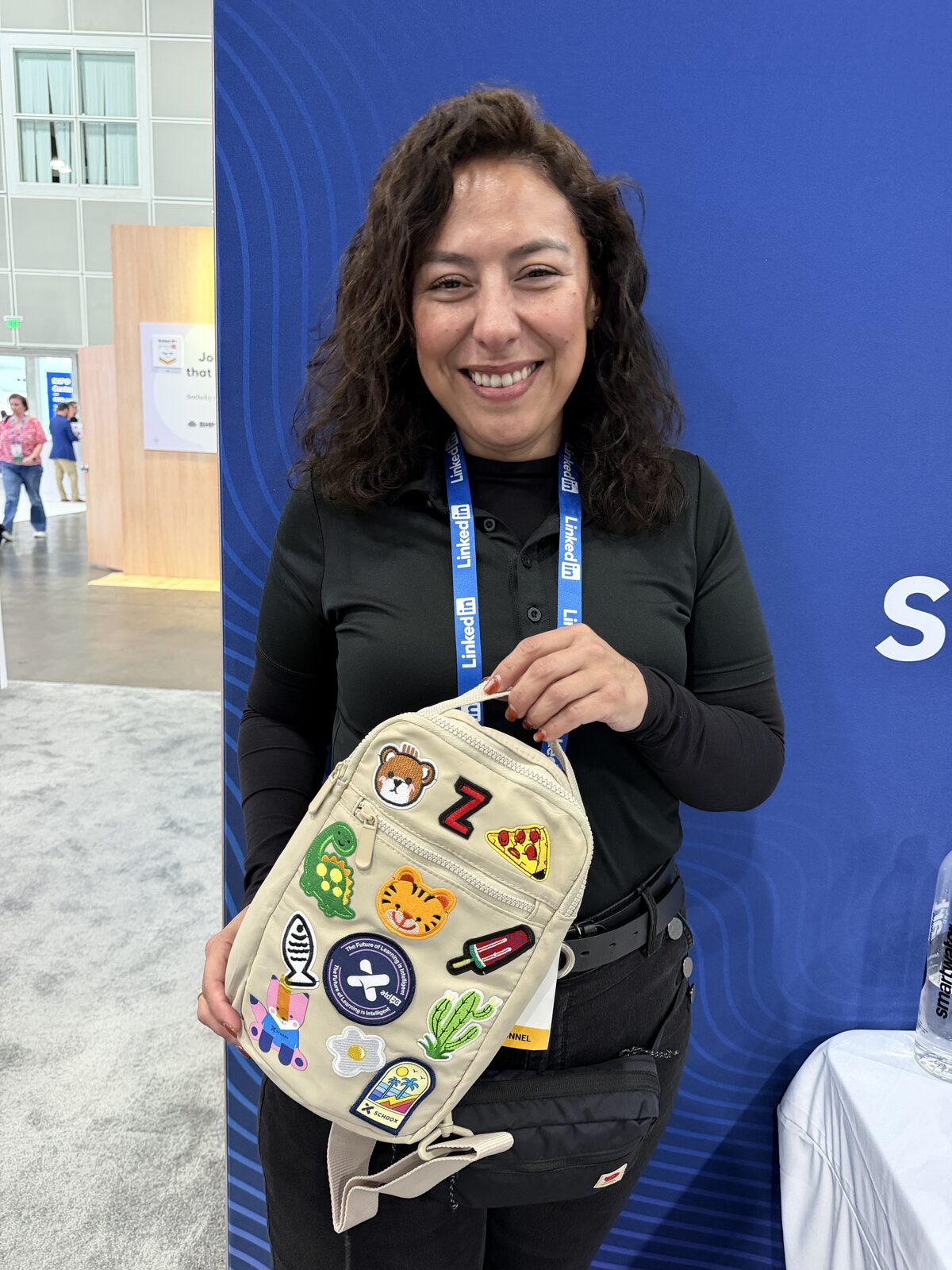 Smiling conference guest holding a canvas mini backpack covered in custom mix-and-match patches from the Custom Patch Bar
